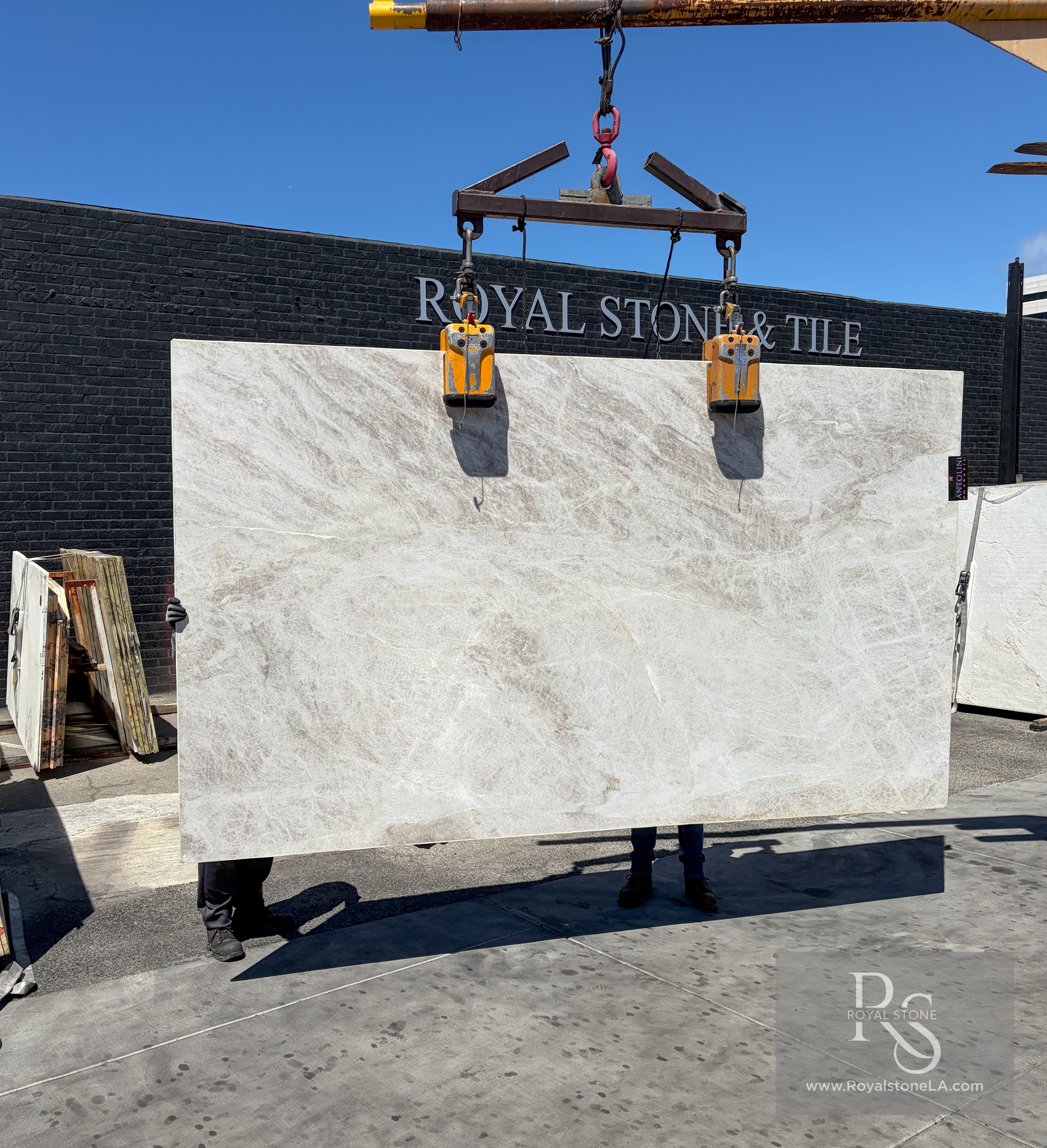 Antolini Taj Mahal Select light-shade quartzite slab, 2cm soft-leathered, 77 by 131 inches, with a pale champagne-ivory field and quiet taupe veining, hanging from a crane at the Royal Stone Los Angeles yard