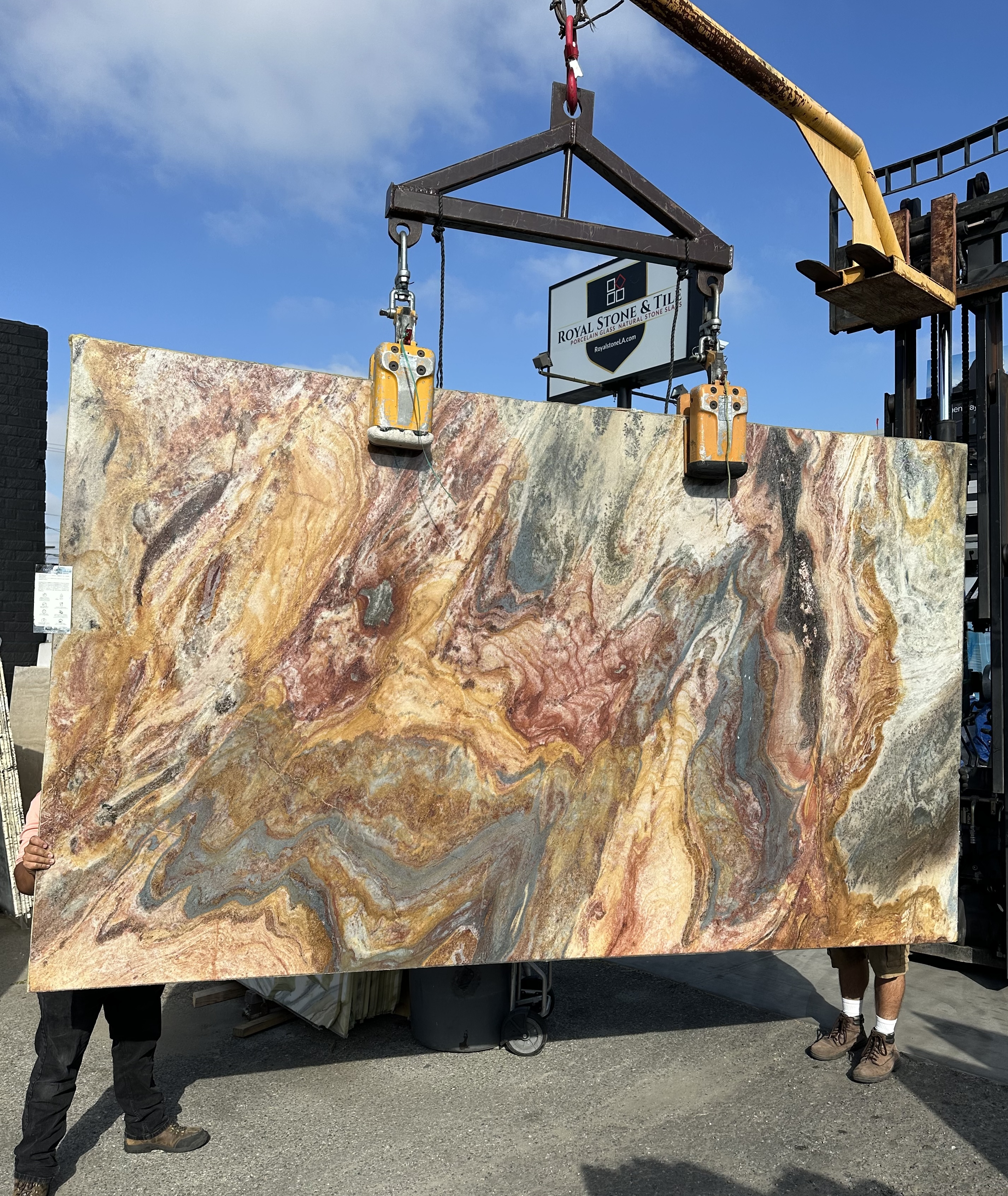Antolini Van Gogh Blue Louise quartzite slab, 2cm polished, 75 by 128 inches, with painterly swirls of amber, gold, rose, slate-blue, and charcoal across a warm field, hanging from a crane at the Royal Stone Los Angeles yard