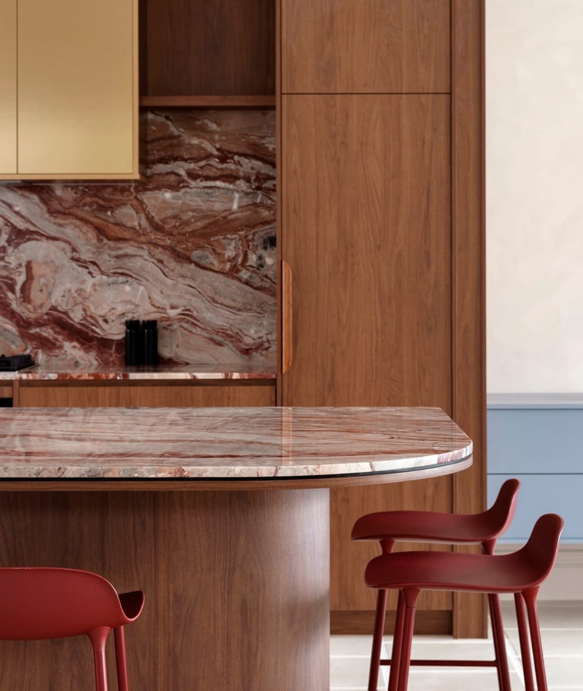 Viola Orobico marble used as a kitchen island top and backsplash, framed in oiled walnut cabinetry with brass detailing and red bar stools