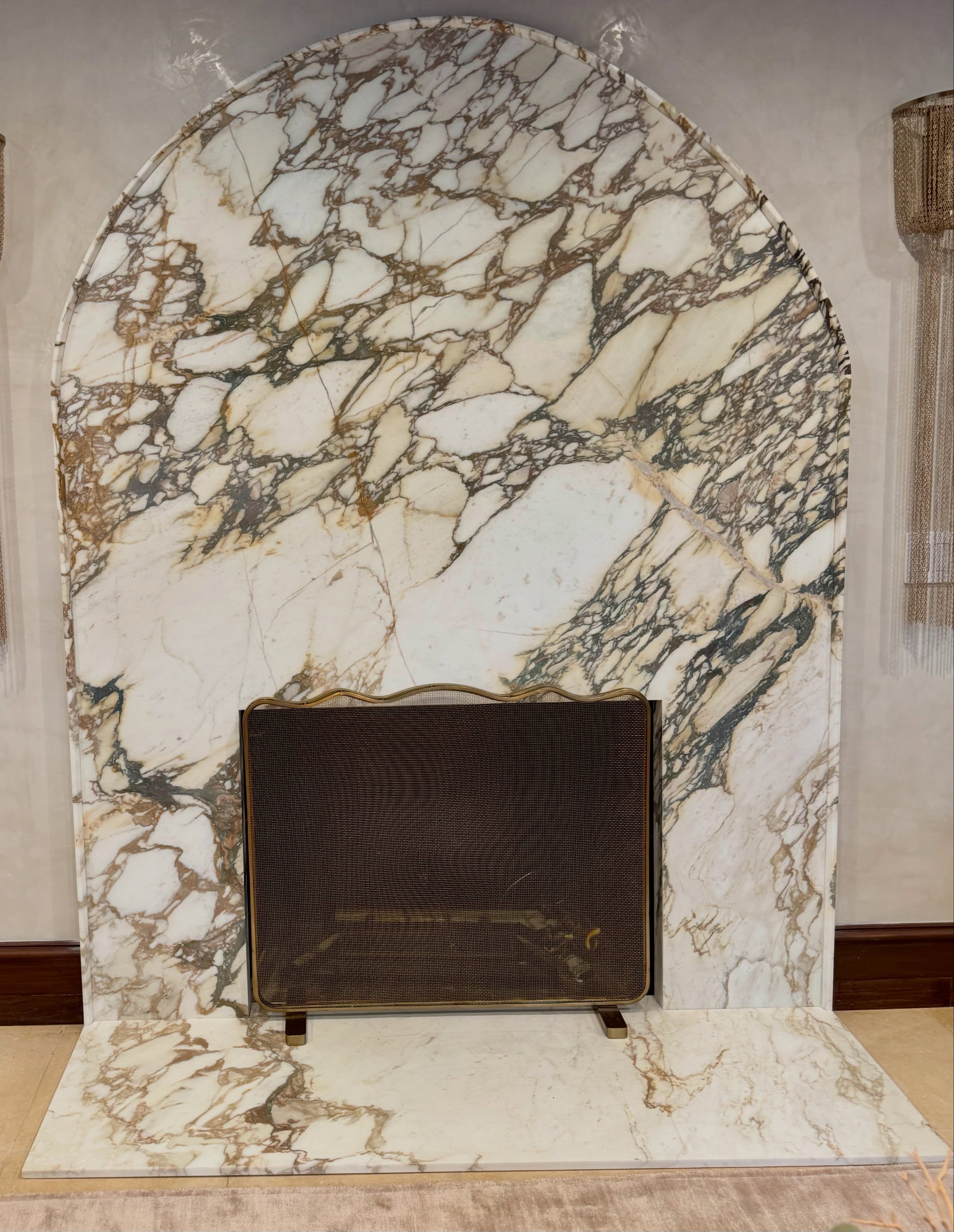 Custom arched fireplace surround and hearth crafted from white and brown natural stone with prominent veining.
