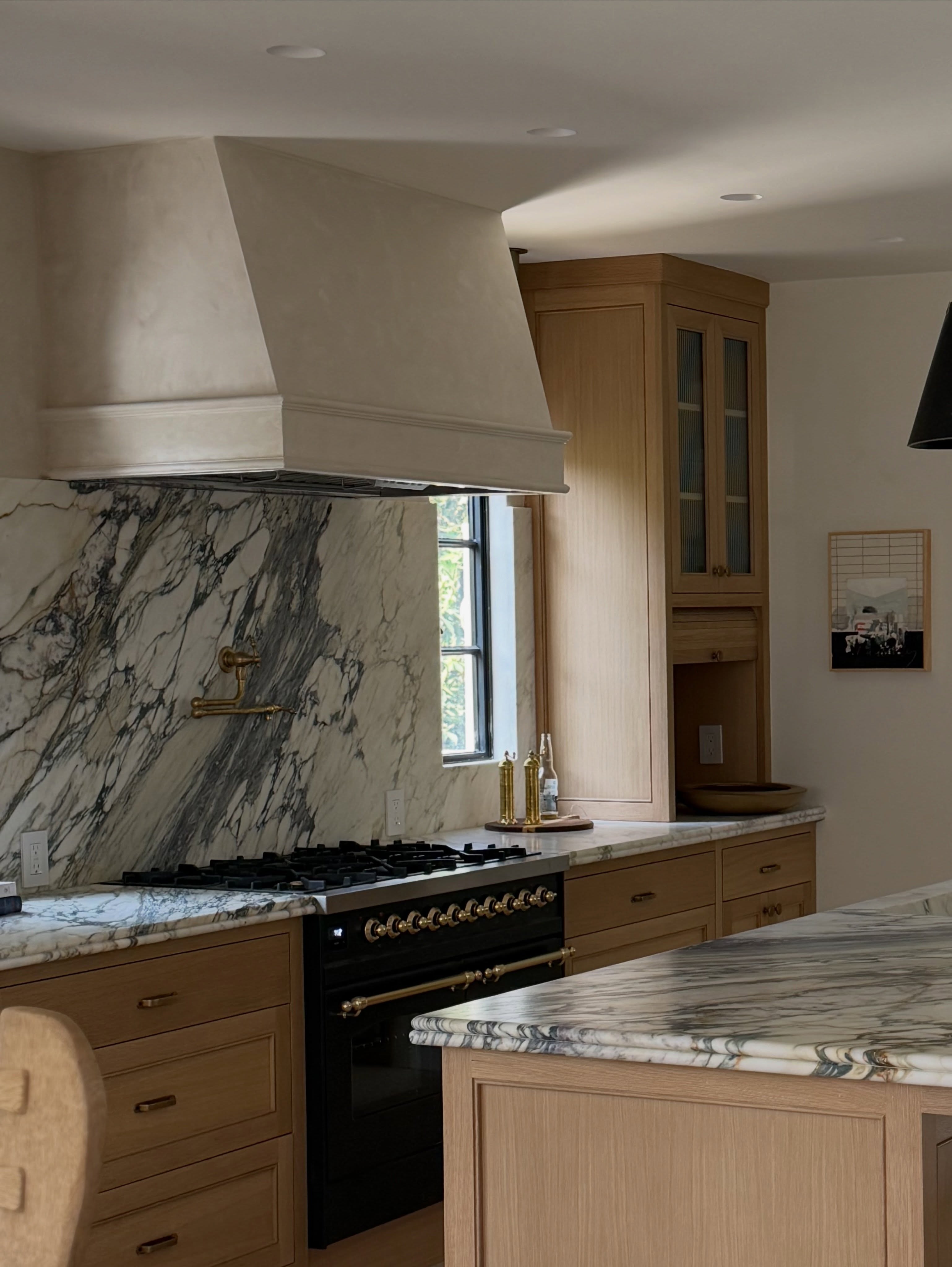 High-end modern kitchen with natural wood cabinetry and dramatic Breccia Capri marble countertops and backsplash.