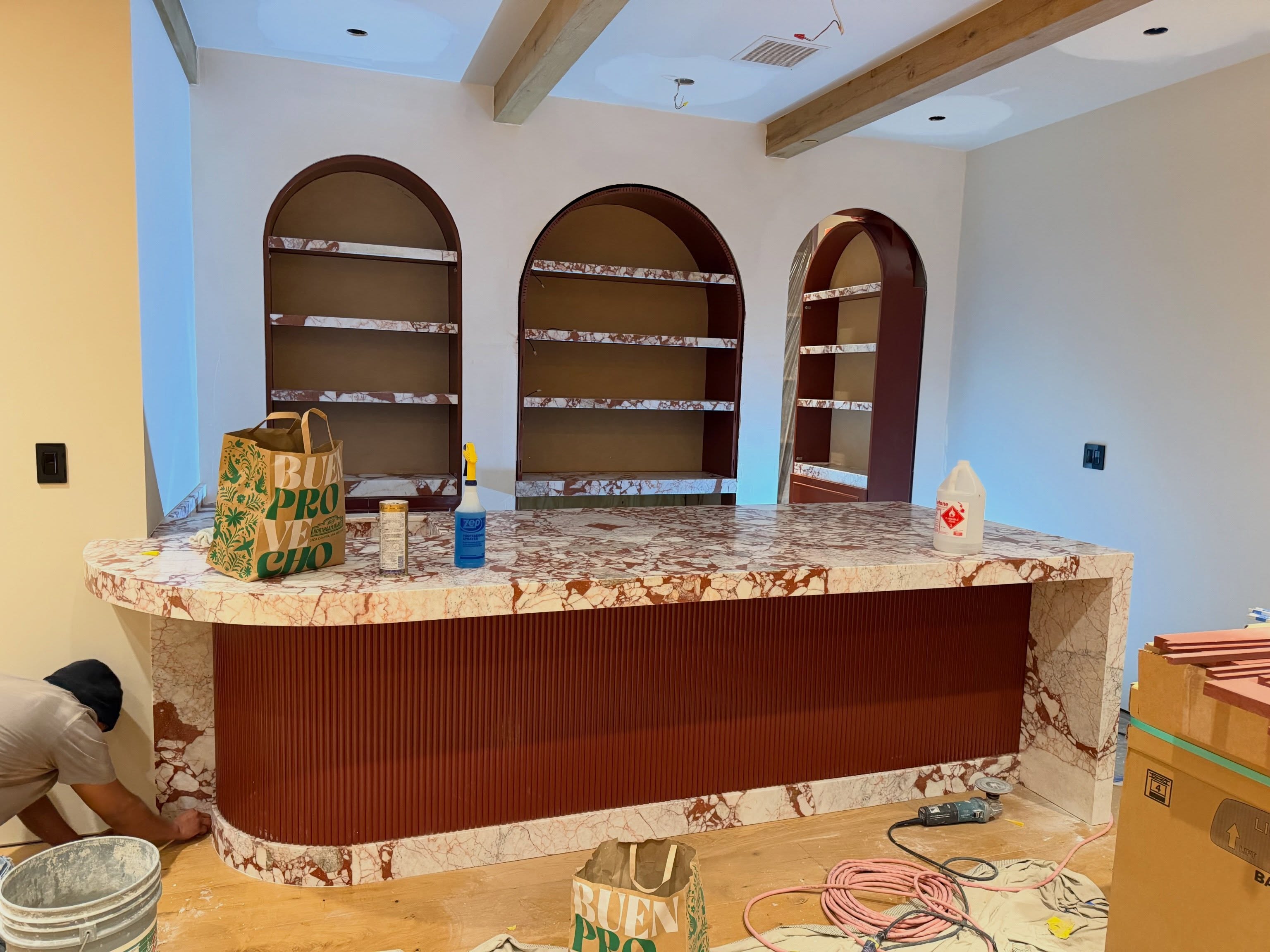 Luxury custom home bar under construction with a Calacatta Rosso marble waterfall counter and matching arched shelving.