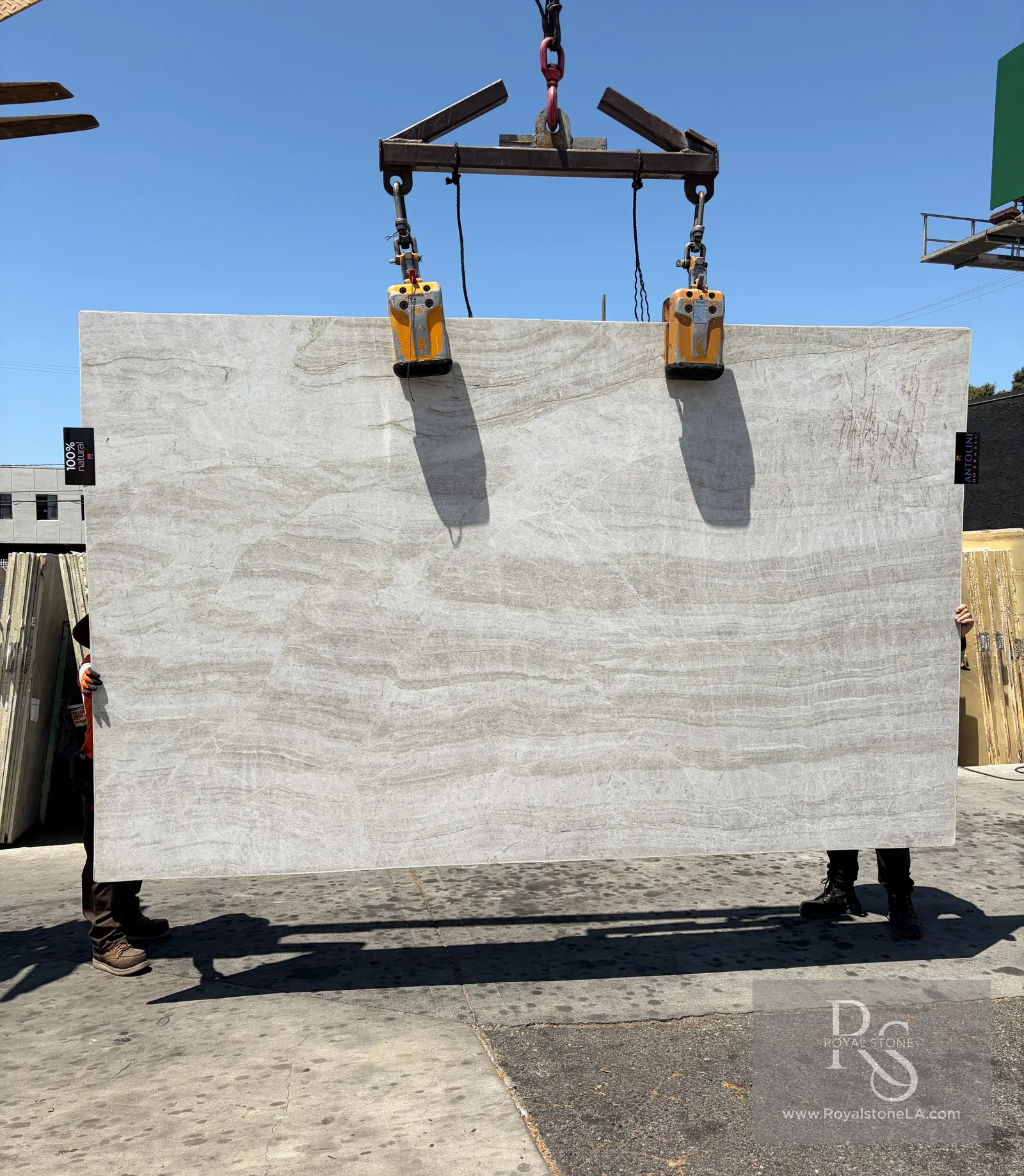 Taj Mahal Select leather-finish quartzite slab at Royal Stone, warm ivory field with horizontal drift, 79 by 130 inches, lifted by overhead clamps in the Los Angeles yard